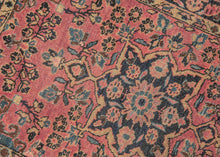 This Sarouk rug was handwoven during the second quarter of the 20th century. 
It features of an deep navy central medallion on a crimson ground. The field is filled with fine floral sprays and balanced by four scalloped cornices woven in light blue. The border is composed of a straightforward floral meander in the same deep navy almost black ground of the central medallion