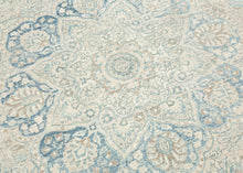 It features an elegant central medallion surrounded by flowing arabesques and floral tracery in delicate shades of sky blue, ivory, and soft taupe. The pale, airy palette and finely drawn design lend the piece a refined, almost ethereal quality that makes it versatile for both traditional and contemporary interiors. Framed by a scrolling vine border, this rug is a study in subtle sophistication and is a timeless decorative element for any space.