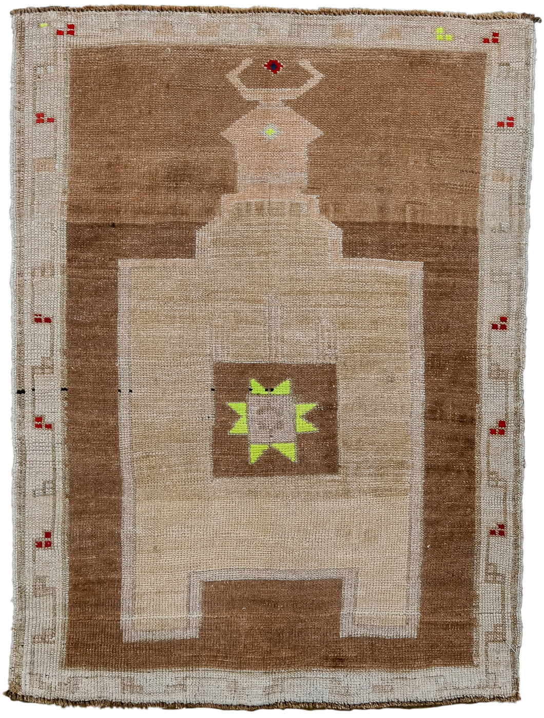 It features a directional camel ground mihrab atop an open chocolate ground. The center of the mihrab features a square in the same chocolate ground filled with an eight pointed star. The star sparkles in a very prominent highlighter yellow. Framed by a simple scrolling cream border with groupings of small red berries and a couple pops of yellow. KARS