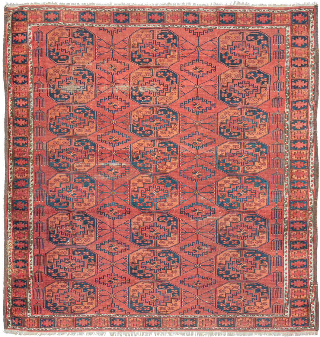 This Ersari Turkmen rug was woven in Northern Afghanistan.  It features a traditional Ersari gül design with a with soft palette of orange and indigo on an earthy madder red ground with accents of natural undyed brown and ivory wool. The secondary guls are more skeletal and interconnected by thin weblike lines. Of particular interest are two columns of amulets on either end of the field which add some distinction and serious interest to this usually straightforward design lexicon.