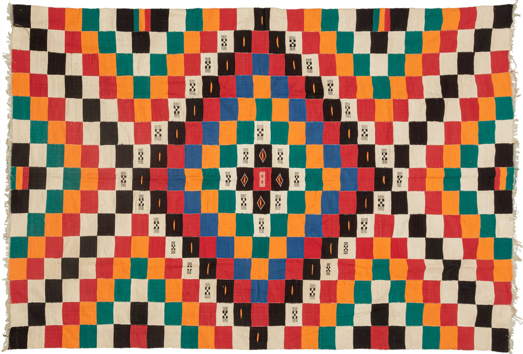 This blanket was likely woven by the Fulani people in Mali during the middle of the 20th century.
It was woven in multiple stripes which have been attached horizontally. It features an eye dazzling checkerboard composed of white, black, red, green, blue and a sunny yellow-orange. Four individual squares around the perimeter are woven with the red-yellow-green tricolor of the Malian flag.
Via The Metropolitan Museum of Art The checkerboard, a basic West African composition, ultimately may derive from