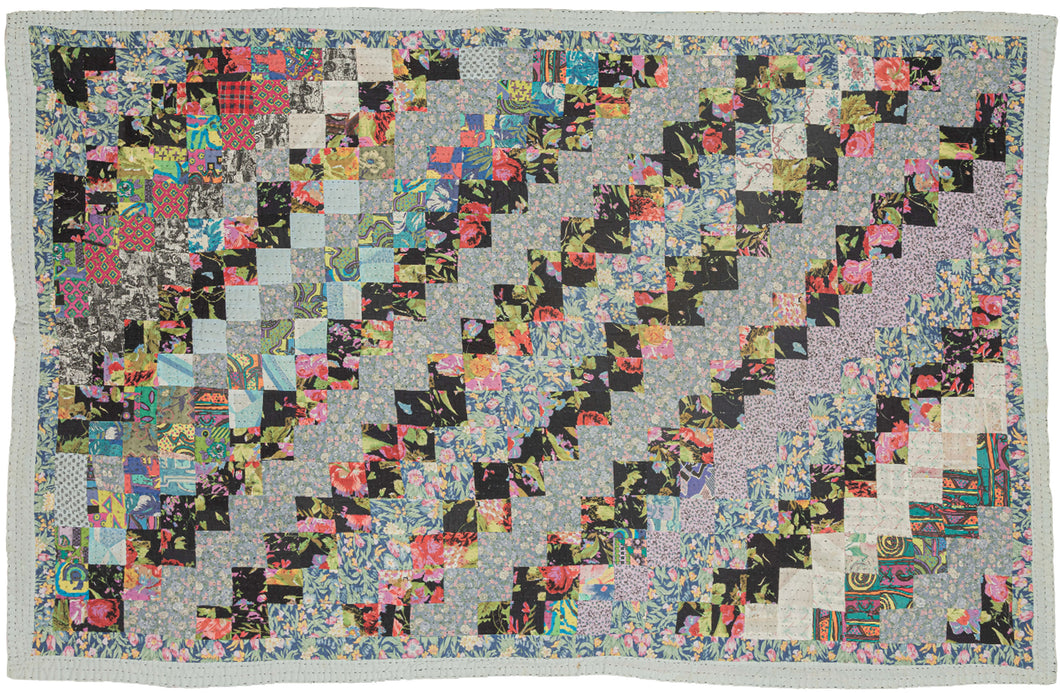 This vintage patchwork quilt was crafted in North America during the middle of the 20th century.
It features patch-worked squares of various fabric in rows of serrated stripes organized on the diagonal. Many of the squares feature there own detailed patterning which adds interest and touch of fun! Much of the stitching has been completed by hand included large visible running stitches in black giving the piece a kantha-like feel.