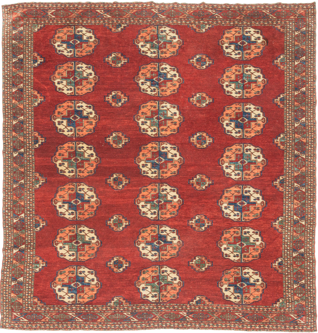 This Tekke main rug was handwoven during the first quarter of the 20th century in Turkmenistan.
The field features a grid rounded main guls in apricot, indigo, turquoise and ivory on vibrant red ground. The space between the grid is filled with rows of cruciform shaped secondary guls. In a rare square format that allows for very luxurious and open spacing of the guls.