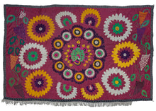 This "1975" Peacock Suzani  features a peacock in all its splendor, embroidered in hot pink, faded green, bright yellow, and purple. A circle of smaller medallions in alternating colors frames the peacock. Larger medallions complete the concentric design. Grape vines are embroidered on either side. There are drawn markings visible where the design was left unfinished in places, highlighting the human hand. The date "1975" is embroidered in hot pink below the central medallion.