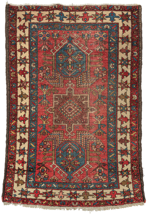 small antique NW Persian Karadja rug featuring a geometric triple medallion design characteristic of the type in blue, pink, yellow, and red with ivory and brown accents. It is framed by a bright ivory main border and flanked by a red outer border and a blue inner border.
