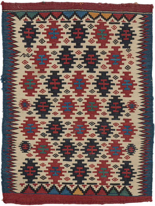 This kilim was woven in the Caucasus during the late 19th century.  It features a field of stepped polygons and small diamonds in various shades of red and blue on a bright ivory ground. The pattern can be viewed multiple way and the navy diamonds also form a central diamond. The ivory field is framed by jagged purple zigzags on the sides and polychrome triangles on the top and bottom and finished with thick bands of blue and red.  May have been made as one side of a saddle bag. A small but impactful piece.