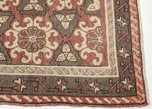 It features a striking allover lattice design with repeating floral rosettes and angular motifs in a balanced palette of earthy terracotta, chocolate brown, ivory, and soft blue. The wide border, decorated with stylized stars and angular vine elements, frames the field beautifully, adding depth and structure to the pattern. The bold yet harmonious composition and soft tones exemplify the sophisticated village weaving traditions of the region.