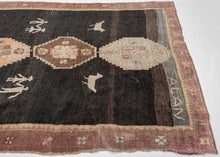 This expressive Kars rug from Eastern Anatolia brings together traditional village weaving with playful, almost naïve figural motifs. Set against a dark brown-black ground, the central row of soft pastel medallions is flanked by charming depictions of birds and pairs of human figures holding hands, giving the piece a narrative and whimsical character.