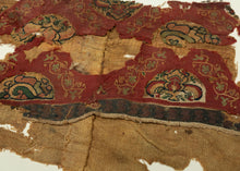 An exceptionally early Coptic textile fragment, woven more than 1,400 years ago, preserving richly patterned tapestry bands against a warm linen ground. Deep red fields are animated with scrolling vegetal forms and inset medallions containing highly stylized floral, animal, and possibly scarab-like motifs in ochre, green, cream, and dark brown.