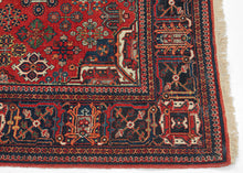 A richly patterned vintage Joshaghan rug with a dense field of highly stylized floral and geometric motifs surrounding a dark indigo diamond medallion. The saturated madder-red ground is enlivened by an unusually broad palette of indigo, sky blue, turquoise, green, ivory, apricot, gold and soft coral.