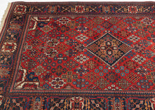 A richly patterned vintage Joshaghan rug with a dense field of highly stylized floral and geometric motifs surrounding a dark indigo diamond medallion. The saturated madder-red ground is enlivened by an unusually broad palette of indigo, sky blue, turquoise, green, ivory, apricot, gold and soft coral.