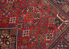 A richly patterned vintage Joshaghan rug with a dense field of highly stylized floral and geometric motifs surrounding a dark indigo diamond medallion. The saturated madder-red ground is enlivened by an unusually broad palette of indigo, sky blue, turquoise, green, ivory, apricot, gold and soft coral.