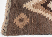 A wonderfully tactile Angora Tulu rug distinguished by its exceptionally soft, shaggy pile and striking geometric composition. Woven in a restrained palette of undyed Angora goat hair, the rug features a rich, earthy field of charcoal brown and warm taupe, punctuated by an ivory central medallion with jagged, irregular contours.