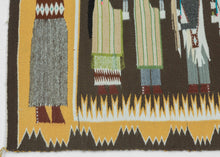 A finely woven Yei Bi Chei pictorial by celebrated Diné weaver Della Woody Begay, depicting a ceremonial procession of masked figures associated with the Navajo Nightway tradition. The dancers are arranged in a rhythmic line between two larger attendant figures, set against a deep brown ground and framed by Woody’s particularly distinctive serrated, cloud-like border.