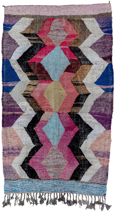 Contemporary Moroccan. This colorful kilim features a central row of totemic polygons flanked zigzags vibrating outwards. In a bright and contrasting palette of blues, reds, pink, purple, yellow, brown black and white. Subtle color shifts add dimension. Finished with horizontal bands on the top and bottom. A classic rag rug made of mixed materials but rendered here in flatweave.