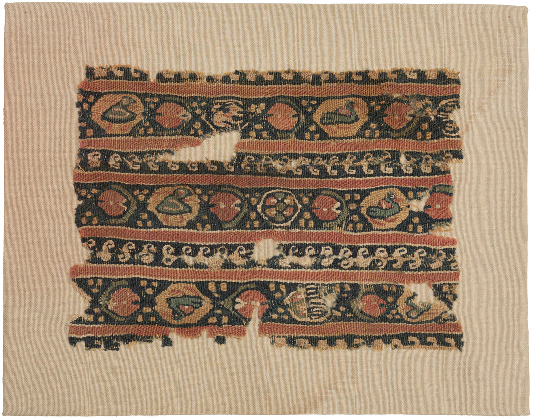 This 8th Century Coptic Fragment features a colorful pattern of striped bands with cartouches alternating between cartouches of ducks and a Pacman-like figure. Smaller rows of scrolling vegetation add additional layers.