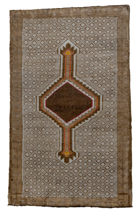 It features a central medallion that floats atop an allover diaond pattern in camel and ivory. The medallion features a open dark chocolate center and contrasting outlines in ivory and red and yellow dashes that add movement and dimension. Framed by a simple and faded camel border. KARS