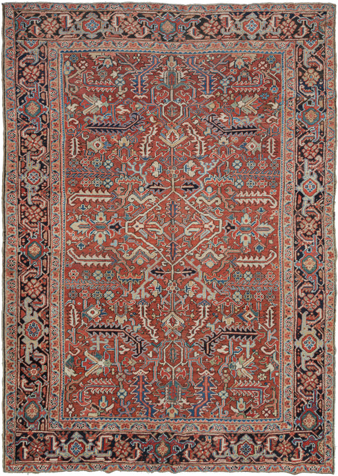 This Heriz rug was handwoven in Northwest Iran during the second quarter of the 20th century.  It features an allover design of geometric palmettes and large serrated leaves in blues, green, coral, gold, black and ivory on an undulating brick ground. All over designs are less common on Heriz rugs which most often feature large central medallions. The main border is composed of a rosette and outstretched arm palmette border on a surmah ground.