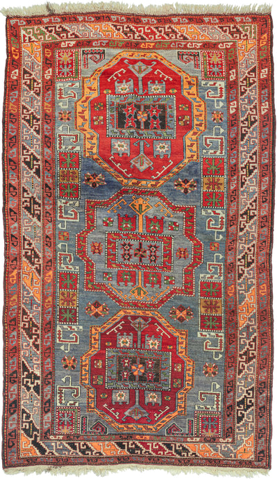 This Kazak rug was handwoven in the southern Caucasus during the second quarter of the 20th Century.  It features three medallions in reds, gold, Ivory, and green on a wonderfully abrashed purply-blue slate ground with a variety of neatly organized protection symbols. The main border is composed of alternating pairs of dragon-like 