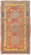 This Khotan rug was woven in Northwest China, which is also known as East Turkestan, during the early 20th century.   This rug features three orb-like medallions of atop a patinated orange-red ground of personality filed palmettes, rosettes and cloudbands. Thick solid color lines frame two main borders. One a wonky greek key on a blue ground in various states of fading and the other polychrome "shou" symbols on a stunning canary yellow ground. Shou is a very auspicious symbol which represents longevity.