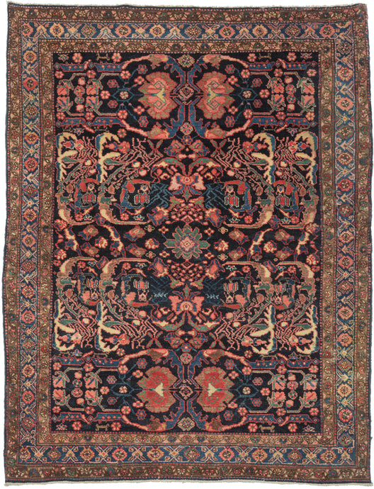 This Malayer rug was handwoven during the second quarter of the 20th century. This stunning rug features a small focal green rosette in the center of a kaleidoscopic design or abstracted vines, leaves and floral forms. Exceptional tones of blue, green, yellow, red coral, and chocolate really pop on the midnight blue ground.  Nicely framed by one main and two minor borders composed of floral meanders, the former more geometric and the latter more naturalistic.  
