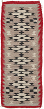 This Navajo rug was handwoven in the Southwest US during the second quarter of the 20th century.  It features interconnected rosette-like diamonds in black and white on a vast gray field. The gray color is created by mixing different strands of undyed wool. The whole is framed by a thin red border that sawtooths into the gray field.