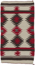 This Navajo rug was handwoven in the southwest United States in the middle of the 20th century.  It features a repeating sunburst pattern in brown, red, and gray on an ivory ground. The pattern features two horizontal bands of solid red and brown in the interior and is finished with solid horizontal bands of gray, brown, and ivory on both ends. 