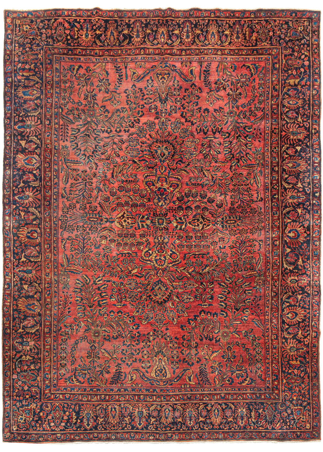 This Sarouk Rug features a curvilinear floral design on a soft raspberry red field. The floral work is intricate and an excellent example of the type of floral sprays Sarouk rugs are known for. It features a central motif that blends into the pattern without dominating the composition. The main border features a palmette and blossom design on a navy ground. This classically patterned rug should last for generations to come.