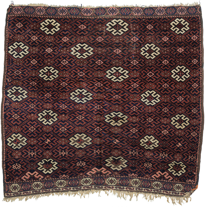 This Baluch rug was handwoven during the first quarter of the 20th century near the border of Iran and Afghanistan.  It features a design of rosette or burr filled diamonds in a lattice format. In tones of madder red, navy, peachy pink and vibrant pops of ivory providing nice nice contrast and visual interest. Finished with multiple columns of selvedge along the sides and finely woven soumak capping the top and bottom. A well balanced and visually intriguing piece.