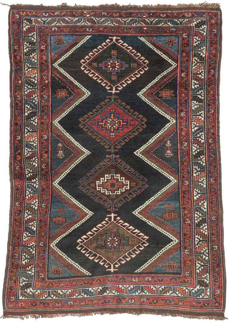 ANTIQUE VERAMIN It features an allover field of four colorful latchhooked diamonds each filled with a memling gul against the deep surmah or blue/black ground and accentuated by striking lightning shaped zigzags. It utilizes a palette of well contrasted, saturated tones including red, orange, multiple blues, greens, brown, and a vivid white that really pops in both the main border and the inner lightning strikes. Nicely finished with extra undyed brown kilim on both ends.