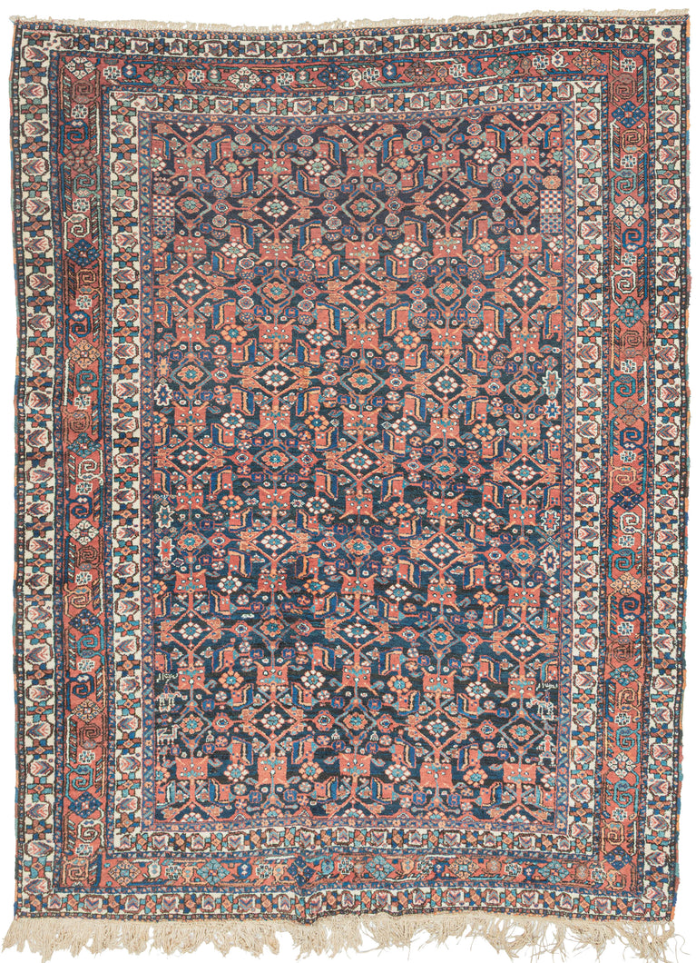 This Afshar rug was handwoven during the second quarter of the 20th century. 

It features an all-over design that is a variation of a herati pattern. The boxy abstracted flowers are rendered in red, orange and turqouise hues on a midnight blue ground. Very figures and talismans can be found hidden amongst the field including a person on horseback and what appears to be the word 