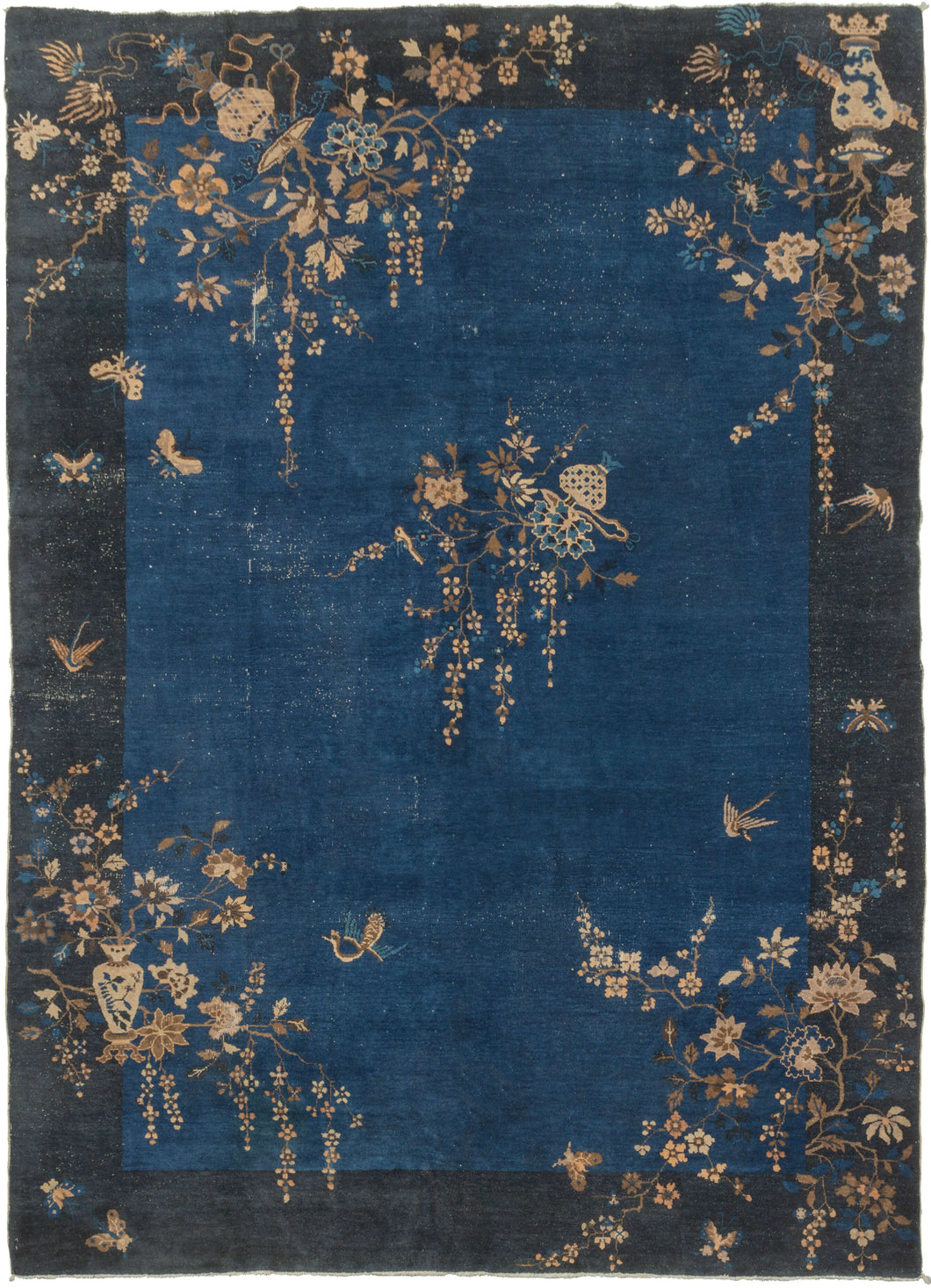 This Deco rug was handwoven in Eastern China during the second quarter of the 20th century.  It features an open indigo field framed by a wide navy border. Flowering vases and branches that start in the border grow freely into the field unrestrained. A flower filled vase with a bird perched on one of its branches can be found near the center of the composition. Various birds and butterflies can also be seen frolicking amongst the flowers