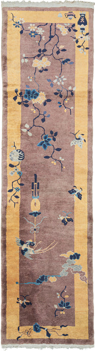 This Yellow and Mauve Deco Runner Rug features a striking contrast of a purple ground encapsulated by a canary yellow border. Various flora and fauna including birds, butterflies and a small flowering tree pay no mind to the barrier between border and field giving this piece a feeling that is free and unrestrained. The bottom left corner features a tea kettle and tea cup next to flowers in a pot. In a hard-to-find runner format.
