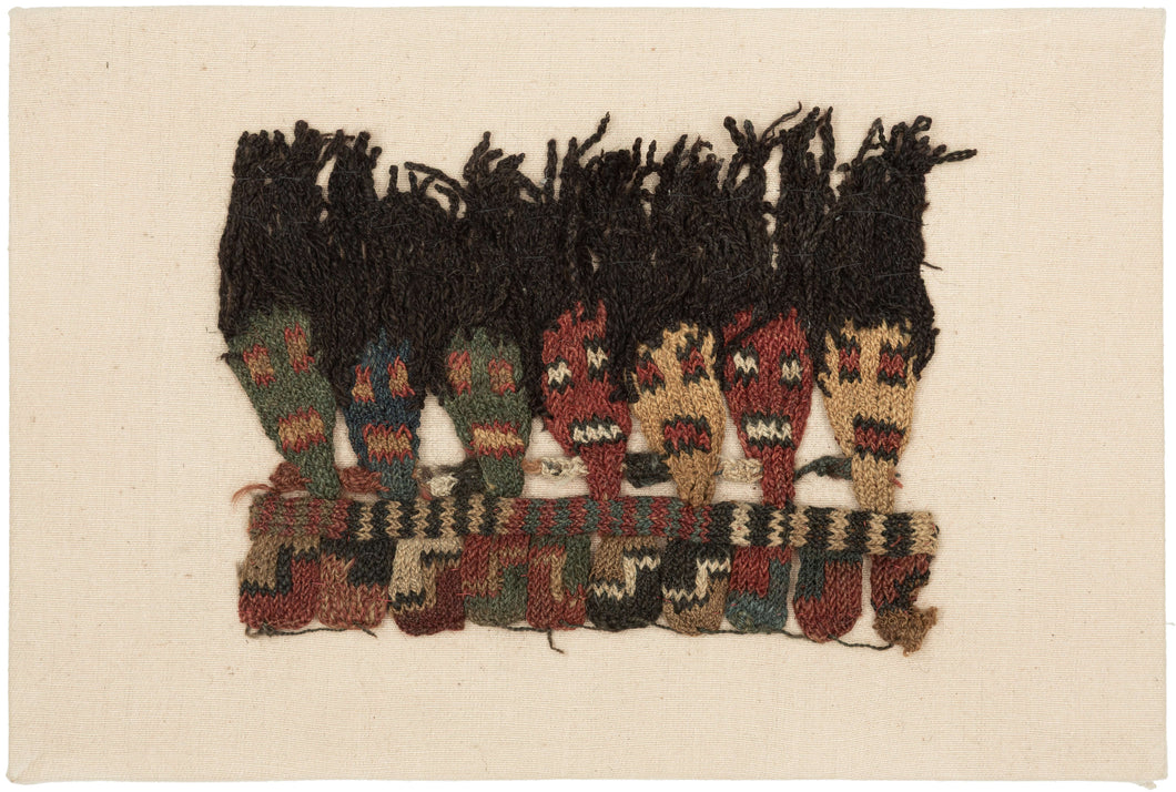 This Pre-Columbian textile fragment dates to the Wari period (circa 600–1000 AD).

It features a striking row of anthropomorphic head motifs with dramatic black wool tufts, likely once serving as the decorative fringe of an elite garment or ceremonial textile. The figures, worked in shades of cochineal red, green, gold, and deep indigo, are a hallmark of Wari iconography and exhibit the sophisticated interlinking knit structure that this Andean culture pioneered.
