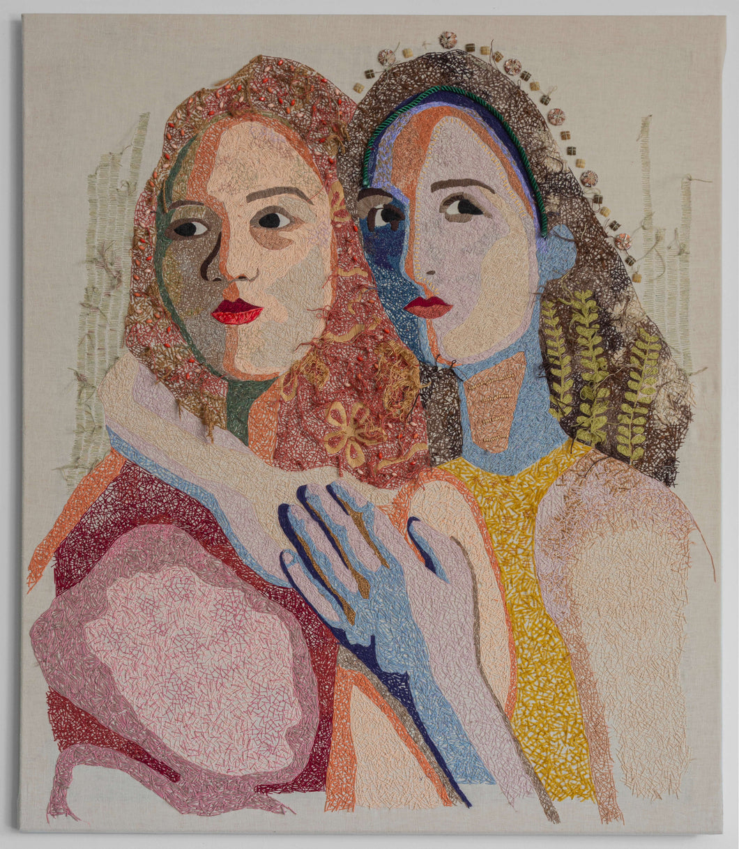One woman warmly embraces another from behind, her hands on top of one another between the second figure's shoulder and heart. The entire portrait is hand embroidered using differing stitching styles. The face combines a satin stitch technique in unexpected color blocks with a more randomized style to create depth and provide a distinction between features. A variety of blues, greens, pinks, purples, and yellows are used in different gradients to surreal effect.