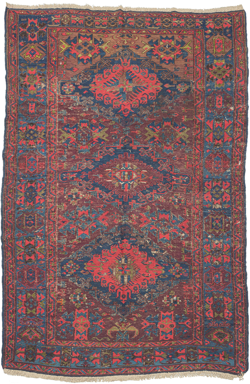 This Soumak features three powerful medallions on an undulating aubergine field. The rest of the palette is composed of vibrant tones of red, cobalt, and hunter-green.  The main border is composed of abstracted palmettes. Nicely finished with the original braided wool fringe.