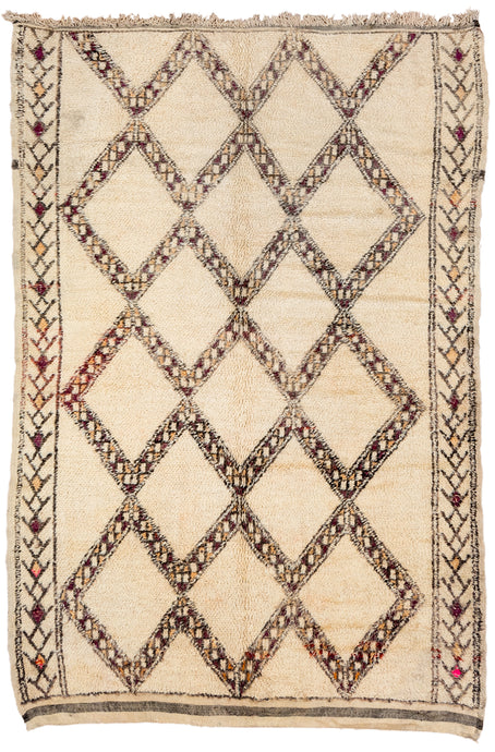 This Beni rug was woven during the late 20th century in the Middle Atlas Mountains of Morocco.  It features a large diamond lattice design in soft purple, yellow and brown on an open cream ground. It is finished simple side borders featuring a simple totemic motif in mostly the same tones other than one moment of hot pink on both sides. The rug is finished with a striped kilim skirt on one end.