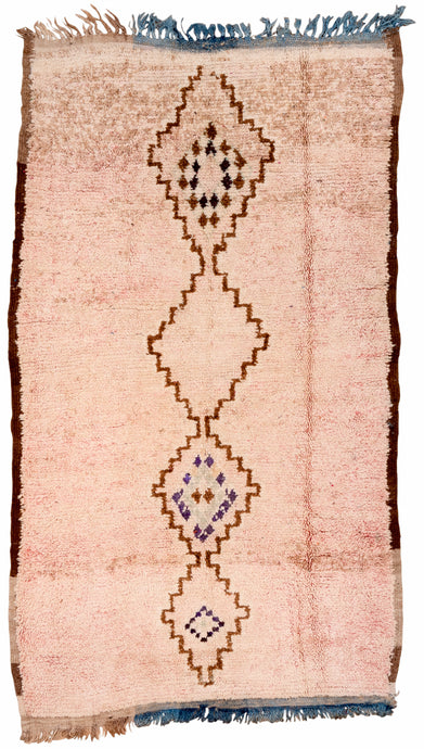 This Azilal rug was woven in the Middle Atlas mountains during the 20th century.  It features a central column of stepped brown diamonds on a pale pink ground. Some are filled with purple and blue diamonds. The addition of some blue to warp adds some fun. 