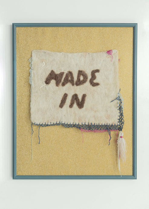 Made In features A light gray hand-felted rectangle with unbalanced needlelace adornments on the borders in pink, blue, and white. The central image is the phrase “MADE IN” spelled in brown felt to mimic the font used by Kim Kardashian’s brand “Skims” which has been known to be manufactured in Turkey despite Kim Kardashian’s connection to the Armenian diasporic community.