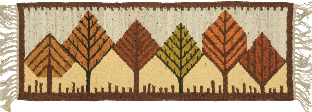 Midcentury Polish Tapestry features a row of abstracted tree forms in various tones of brown orange, green and yellow likely representing the autumn foliage. Below the trees is a soft yellow ground while above the trees the ground is marled gray which is a common shade used in this type.