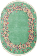 This Oval Chinese Deco Rug features an open field of seafoam green. Its unadorned center is surrounded by an oval ring of various multicolored blossoms. Single rosettes adorn the outer perimeter of the oval ring.  In very good condition, with full even pile. Pile is thickly woven and medium height, with a sturdy handle. 
