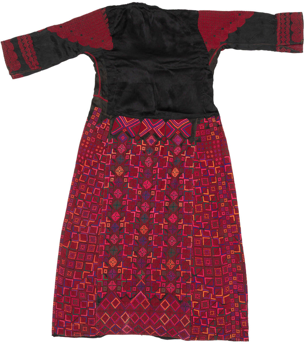 A bold and finely worked Palestinian thobe from the Ramallah–al-Bireh region, distinguished by its saturated red embroidery set against a dark ground and its highly structured, architectural composition.

Dense geometric embroidery covers the skirt, sleeves, and shoulders in tightly organized grids of stepped squares, lozenges, and subdivided diamonds. Vertical embroidered panels frame the body, while the chest features a strong triangular yoke above three square motifs, a characteristic layout associated w