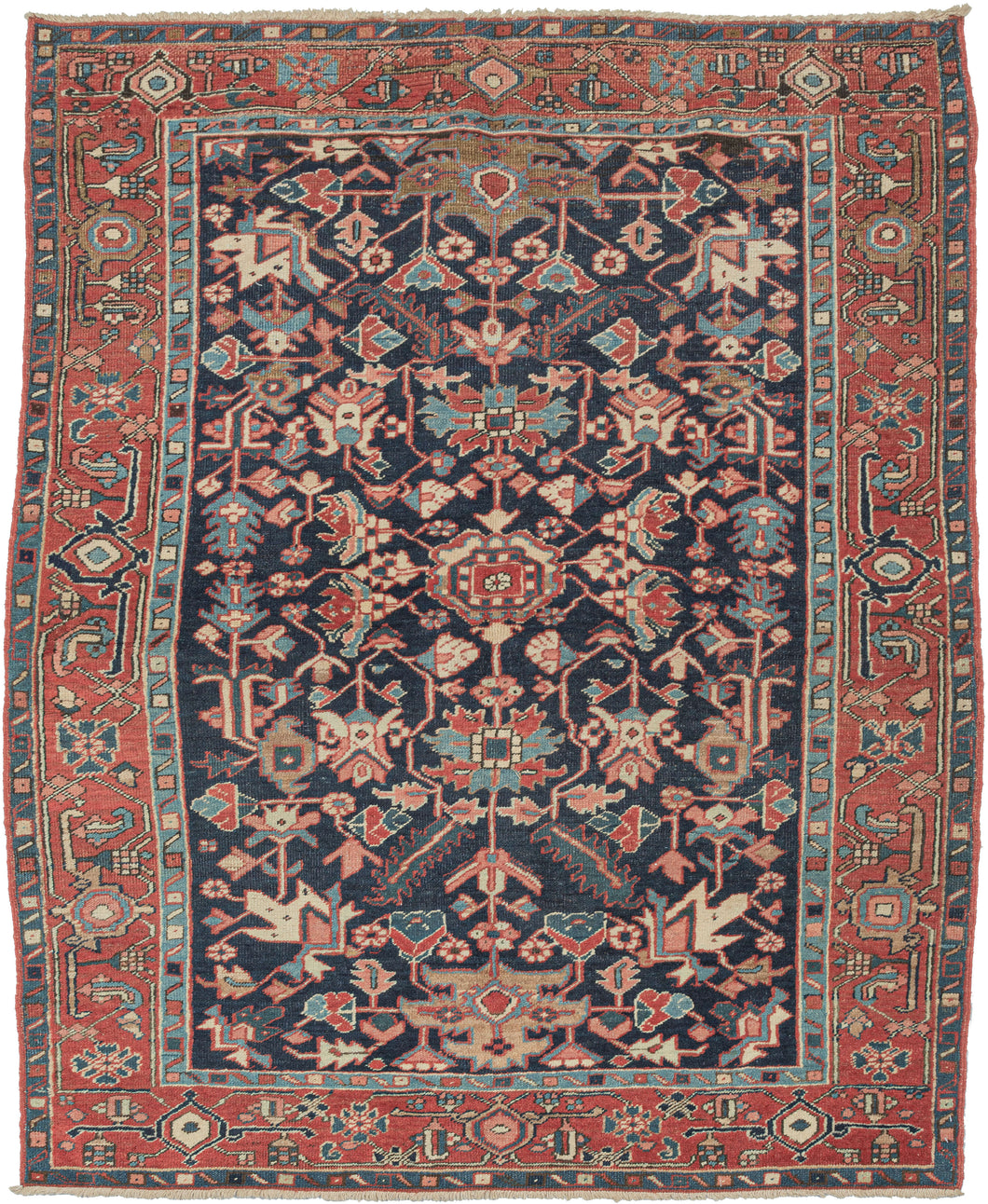 This Heriz rug was handwoven in Northwest Iran during the early 20th century.  It features a well balanced and graphic all over design in green, teal, brick, beige, gold and coral on a dark navy ground. distinctive blue to great visual effect. As most Heriz rugs come in large room sizes, this is a hard to find format. The addition of the less common all over pattern and rare blue ground 