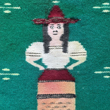 A charming mid–20th century Zapotec weaving from Oaxaca, Mexico, depicting a standing female figure in traditional dress. She wears a wide-brimmed red hat, a white blouse with puffed sleeves, and a striped skirt rendered in earthy tones. Her bold black hair and expressive features are woven with striking clarity, giving the figure a distinctive presence. Metal thread has been utilized in accents of the hat.

