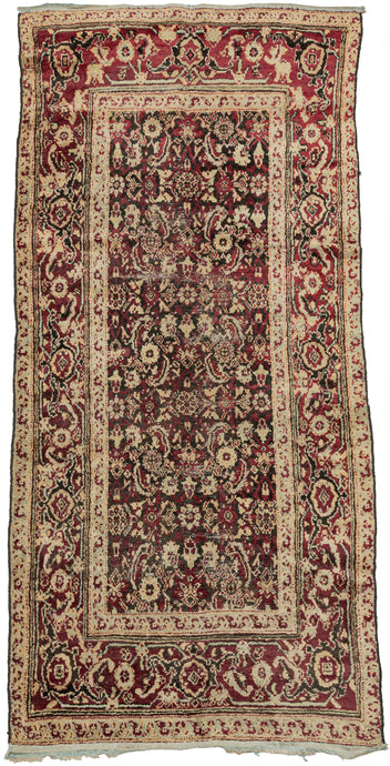 This Agra rug was woven in Northern India during the late 19th century.  It features an elegant all-over herati design in crimson and icy blue on an oxidized brown ground. The crimson tone utilizes lac which is a dye derived from insects and characteristic of Northern India weaving from both Amritsar and Agra. The whole is framed by a reconciled palmette border. A portion of foundation is visible revealing that the underlying cotton has been dyed with indigo.