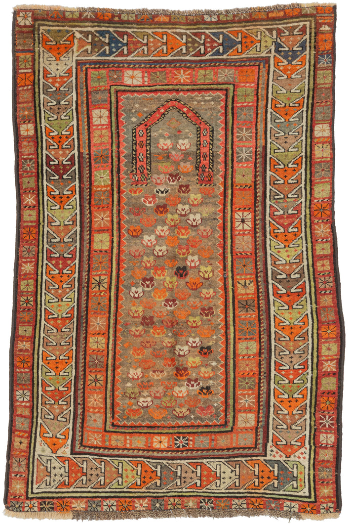 Antique Kuba prayer rug with a geometric mihrab arch and a densely patterned field of small colorful boteh motifs, framed by multiple angular borders in coral, ivory, and green tones.