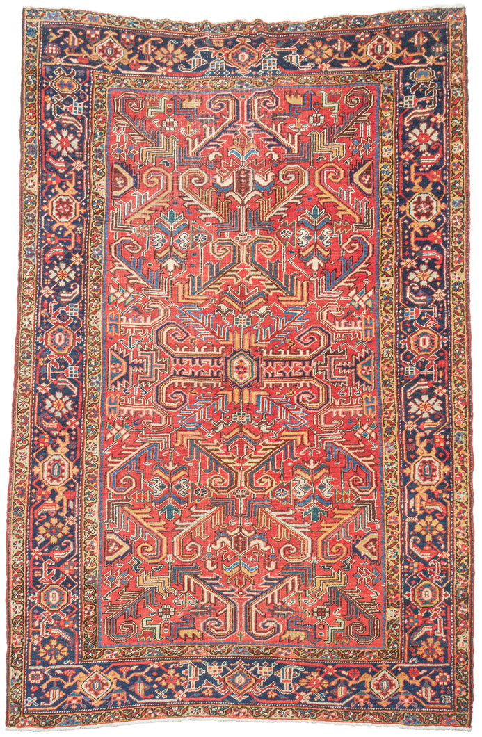 This Heriz rug was handwoven during the second quarter if the 20tb century. 

It features an allover field filled with branching angular motifs, stylized palmettes, stepped forms, and curling leaves radiating around a compact medallion. The palette is warm and vibrant, anchored by a rich madder-red ground accented with deep indigo, sky blue, saffron and ivory. The contrast between the crisp drawing and saturated dyes gives the rug a powerful architectural presence without feeling heavy. A beautifully d