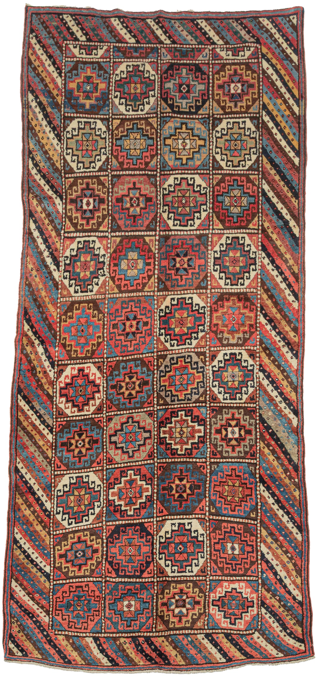 A boldly patterned antique Kurdish long rug woven with a striking compartment design. The field is organized into a grid of stepped, octagonal Memling guls, each enclosing a central rosette, rendered in a rich palette of madder red, indigo blue, ivory, soft camel, brown, and green.

The Memling gul, an ancient geometric motif appearing across many Caucasian and Kurdish weaving traditions, gives the rug its powerful visual structure. Here, the repeated guls are framed by an especially lively diagonal-striped