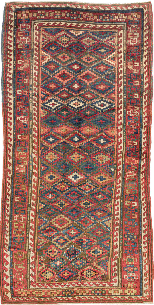 &nbsp;A striking antique Sauj Bulagh long rug, woven by Kurds. The field is densely patterned with offset rows of stepped diamond medallions in saturated tones of madder red, indigo blue, soft ivory, teal green, and warm camel against a rich brown ground.

Sauj Bulagh rugs are particularly admired for their bold color and powerful village drawing. This example has an especially lively allover composition, with each stepped medallion carrying a small central cross form, creating a strong sense of movement ac