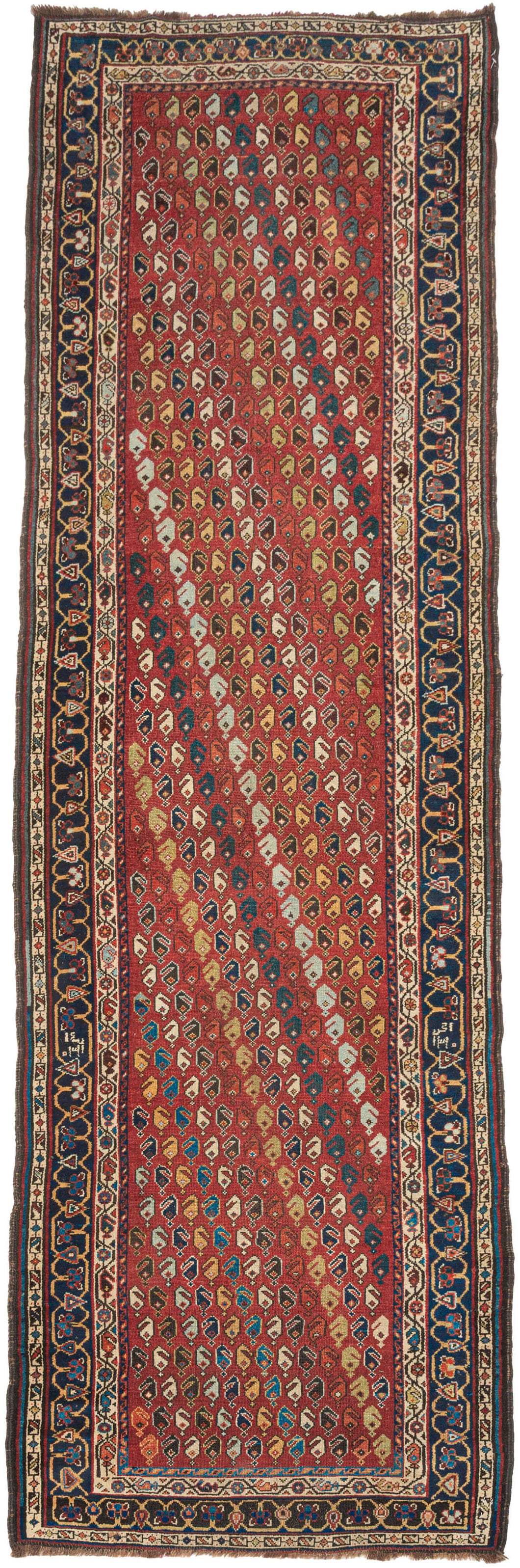 A&nbsp;madder red field densely packed with an all-over diagonal boteh repeat in ivory, navy, gold, teal, and brown forms scattered across the ground in a loose, lively arrangement. The runner reads almost like a textile print at distance and reveals real drawing up close. No two botehs are identical; the color varies row to row, giving the field a warm, animated quality that a more regimented repeat couldn’t achieve.

The main border is a deep navy with a bold reciprocal leaf-and-vine pattern, framed by na